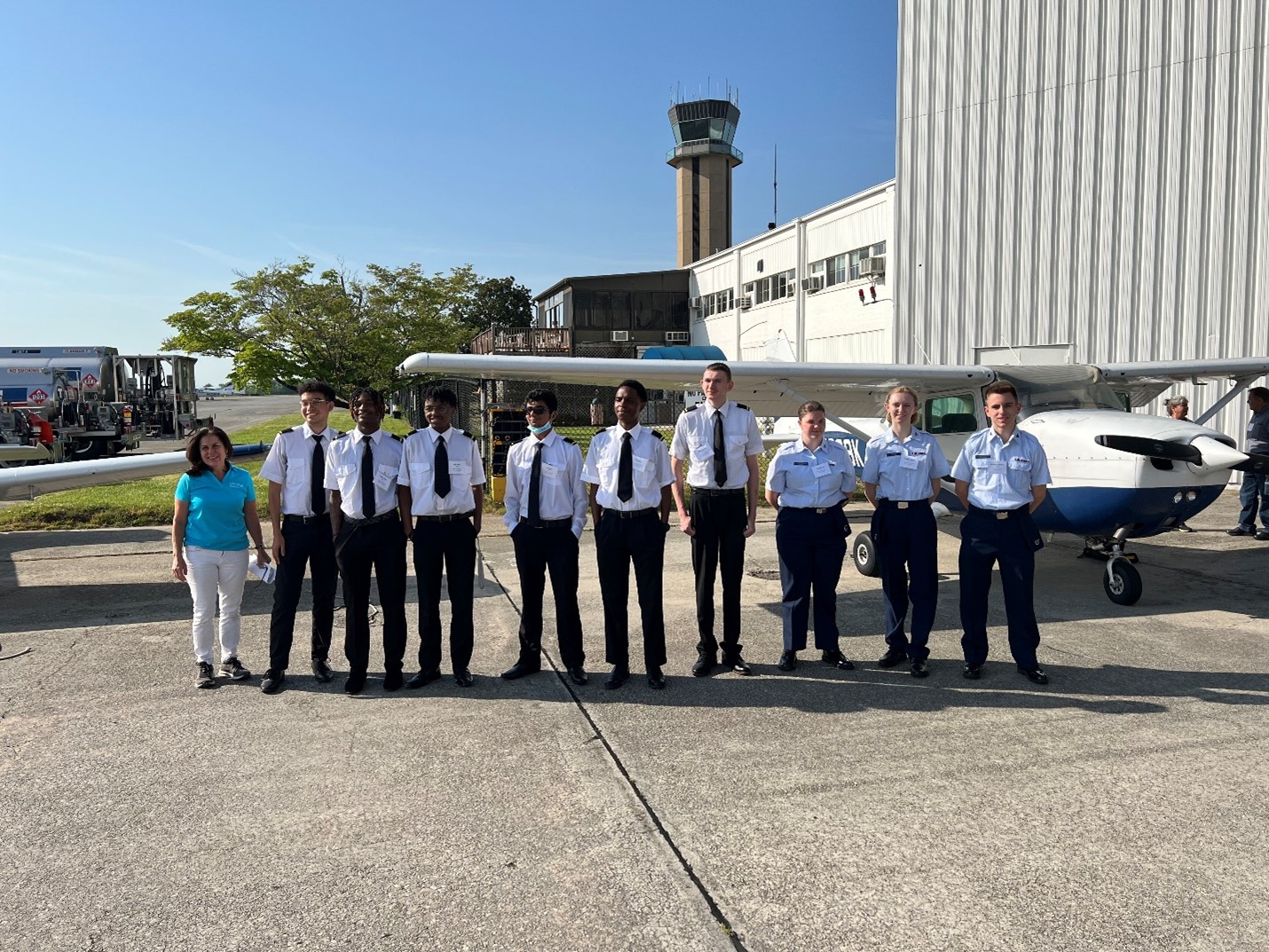 Group of high school students in uniform with Elaine Epps standing outside next to an airplane.