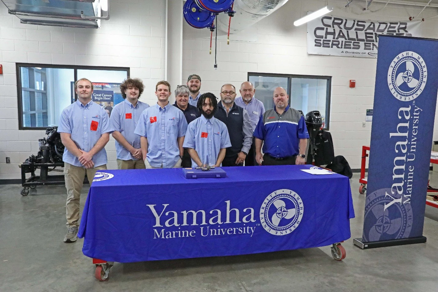 Students standing behind tables draped with the Yamaha Marine University logo.